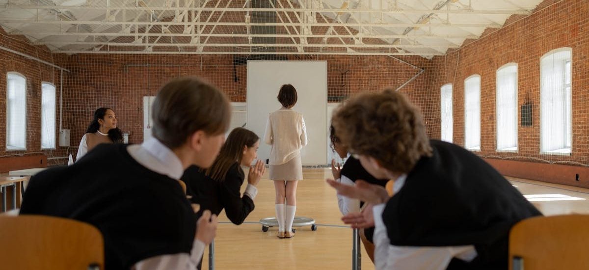 A classroom scene with students gossiping while the teacher stands at the front.