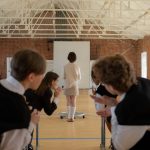A classroom scene with students gossiping while the teacher stands at the front.