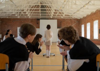 A classroom scene with students gossiping while the teacher stands at the front.